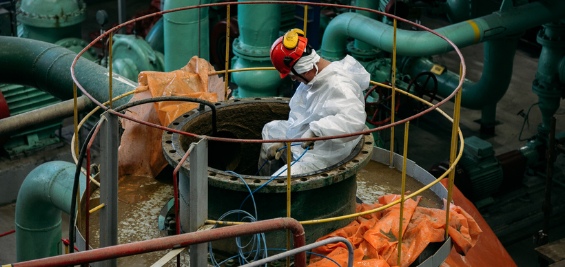 Worker repairs pipe connections of large steel tank