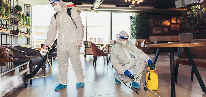 Professional workers in hazmat suits disinfecting indoor